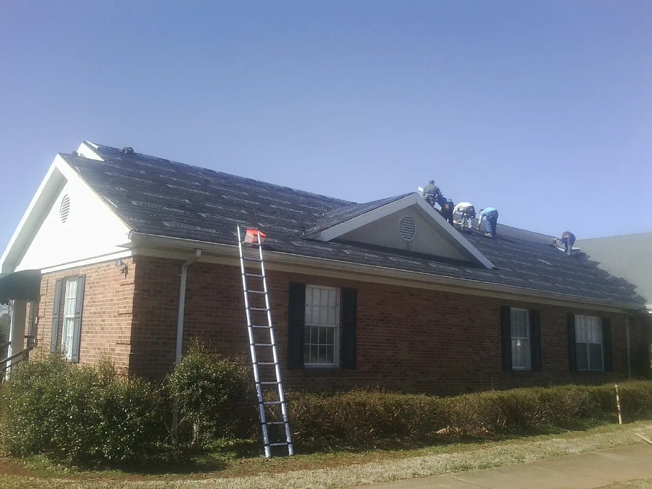 Crew tearing shingles off a brick ranch roof with a ladder set — Emergency Roof Repair work by our crew in Harrington