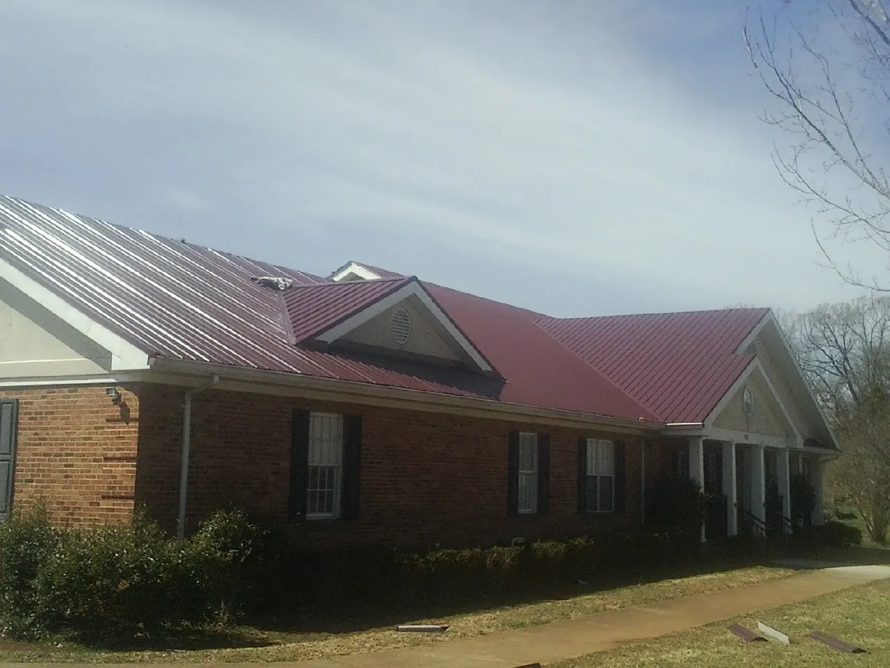 Red metal roof with gabled entries on a long brick building, from a Hail Damage Roof Repair job in Harrington
