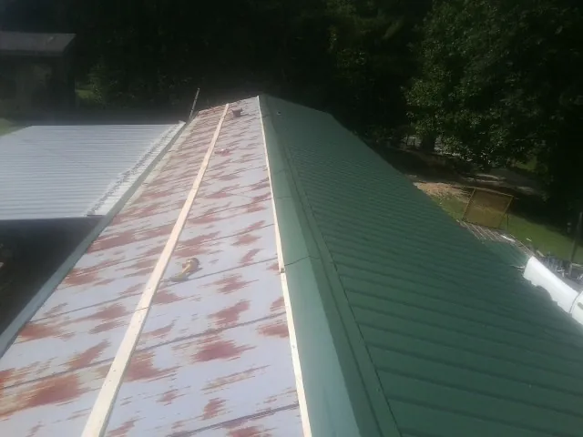 Old rusted panels beside newly installed green metal roofing — Wind Damage Roof Repair by Roofing Brothers in Harrington