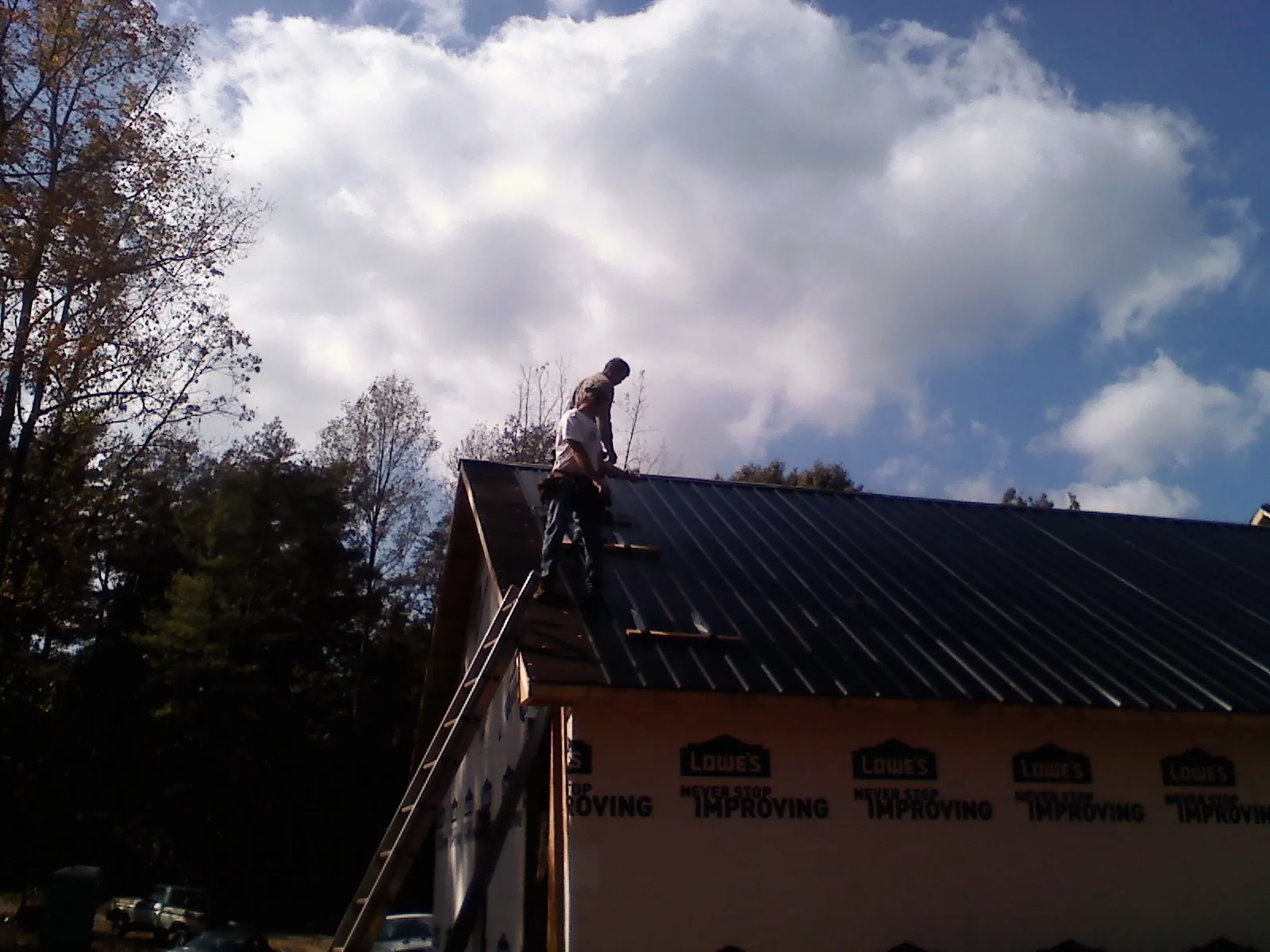 Roofer fastening dark metal panels high against a cloudy sky, from a Roof Inspection job in Harrington