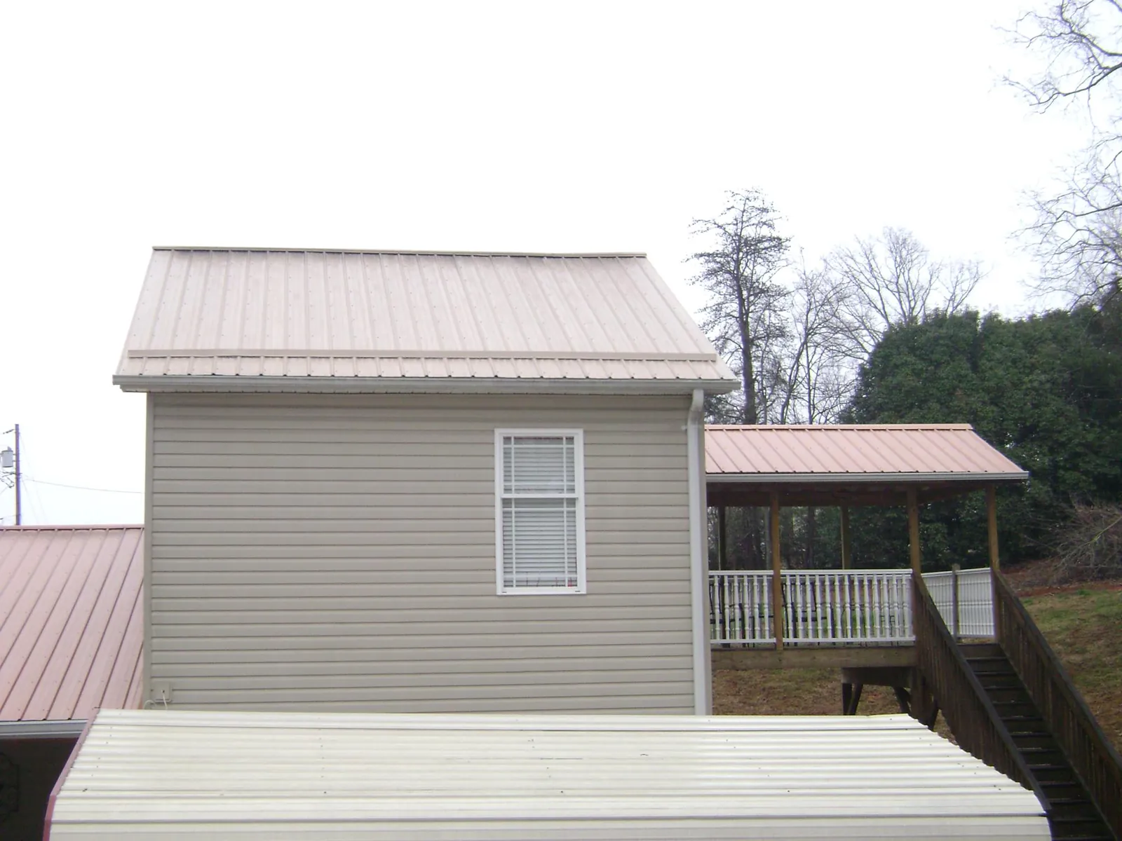 Tan metal roofs on a two story addition and attached porch, from a Roof Replacement job in Harrington